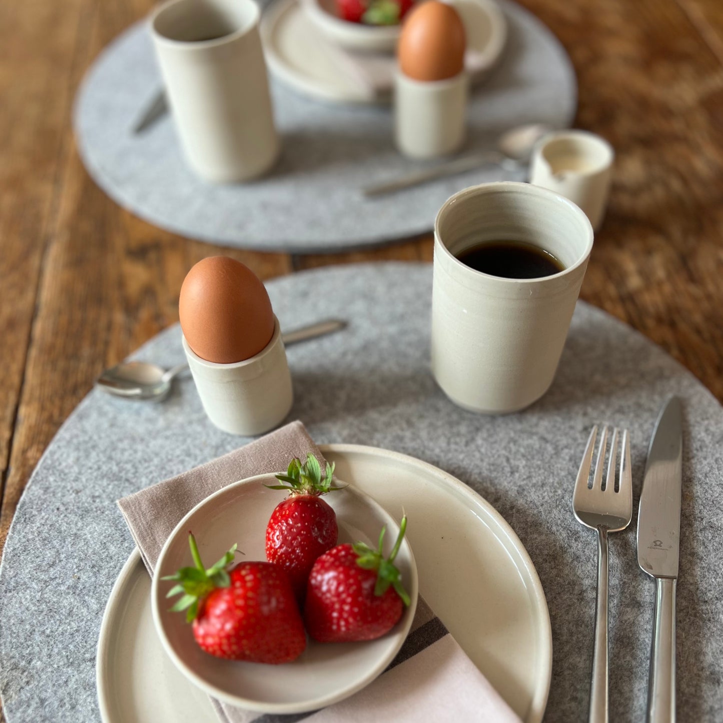zwei beigefarbene handgedrehte Espressotassen aus Steinzeugton auf einem Frühstückstisch, als Eierbecher genutzt