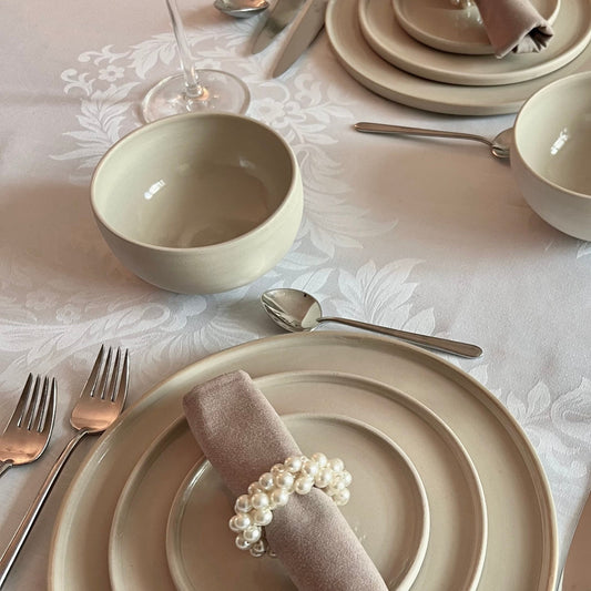 zwei kleine beigefarbene handgedrehte Bowls aus Steinzeugton auf einem mit passendem Geschirr festlich gedeckten Tisch