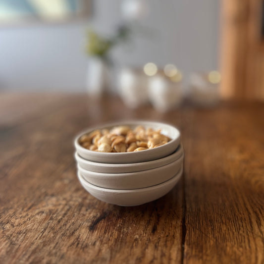 vier kleine beigefarbene handgedrehte Schälchen aus Steinzeugton, gestapelt, die oberste mit Nüssen gefüllt