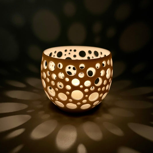 im Dunkeln aufgenommenes Porzellanlicht mit vielen sehr eng liegenden unterschiedlich großen Löchern aus dem eine Kerze ein sehr gemütliches Licht wirft