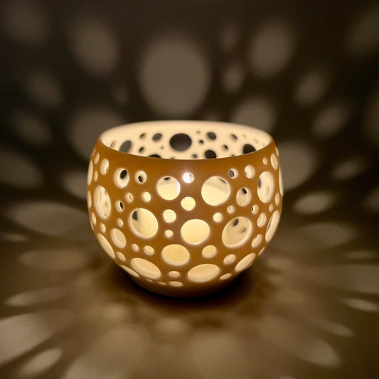 im Dunkeln aufgenommenes Porzellanlicht mit vielen sehr eng liegenden unterschiedlich großen Löchern aus dem eine Kerze ein sehr gemütliches Licht wirft