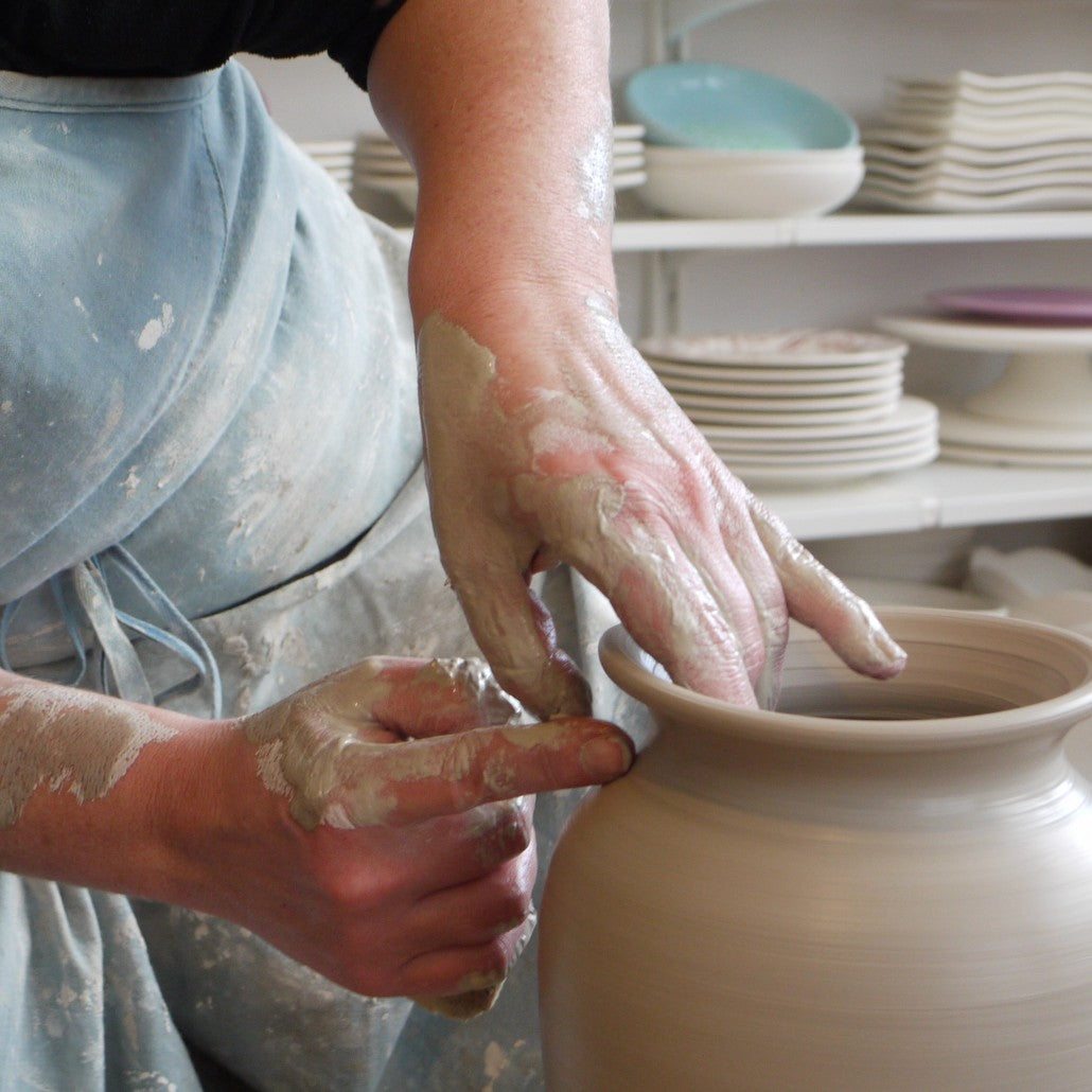 die Hände einer Keramikerin, die eine große Vase auf einer Scheibe dreht