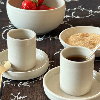 zwei beigefarbene handgedrehte Espressotassen aus Steinzeugton auf passenden Untertassen neben Zucker- und Obstschälchen