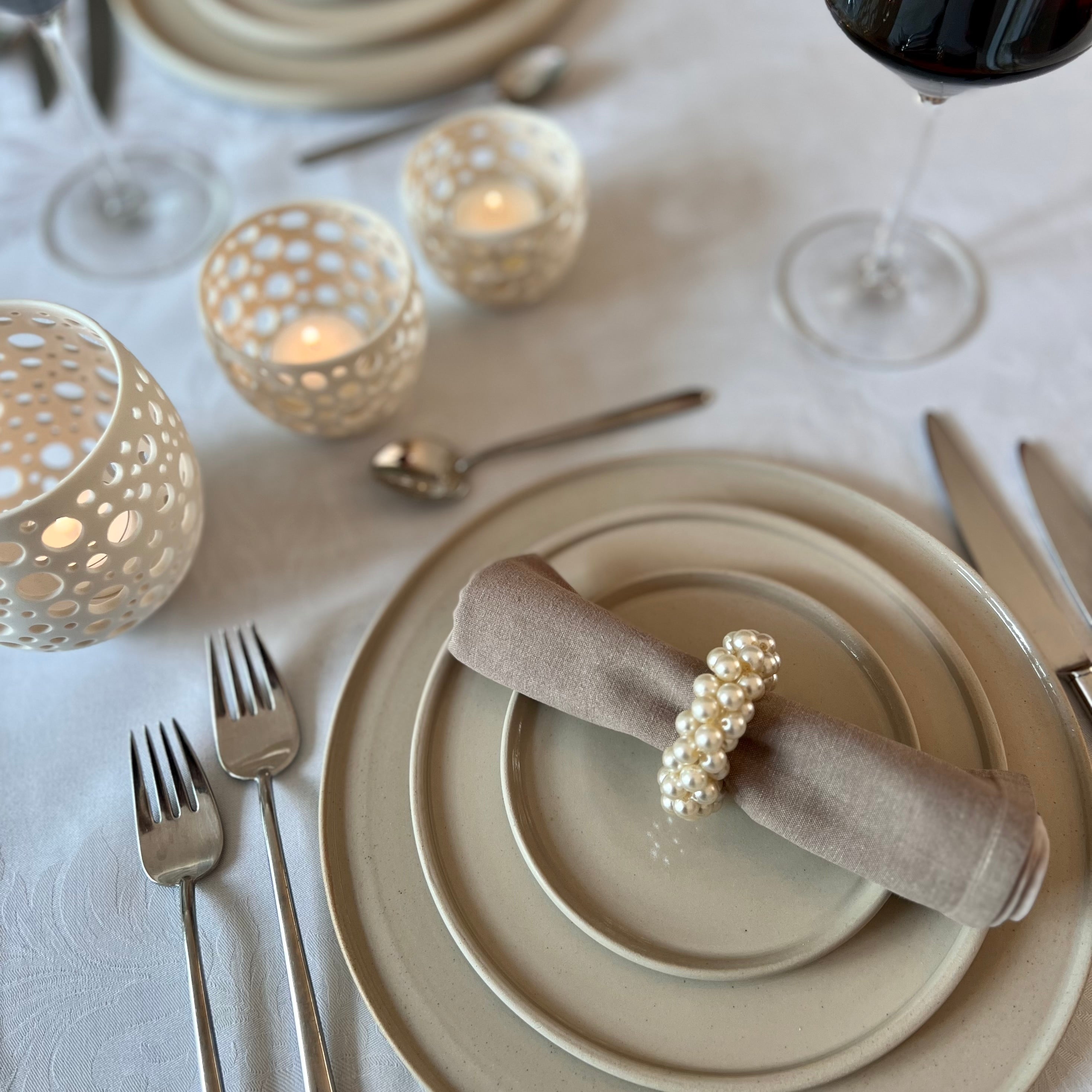 ein mit handgedrehtem Geschirr festlich gedeckter Tisch mit Porzellanlichtern und Weingläsern