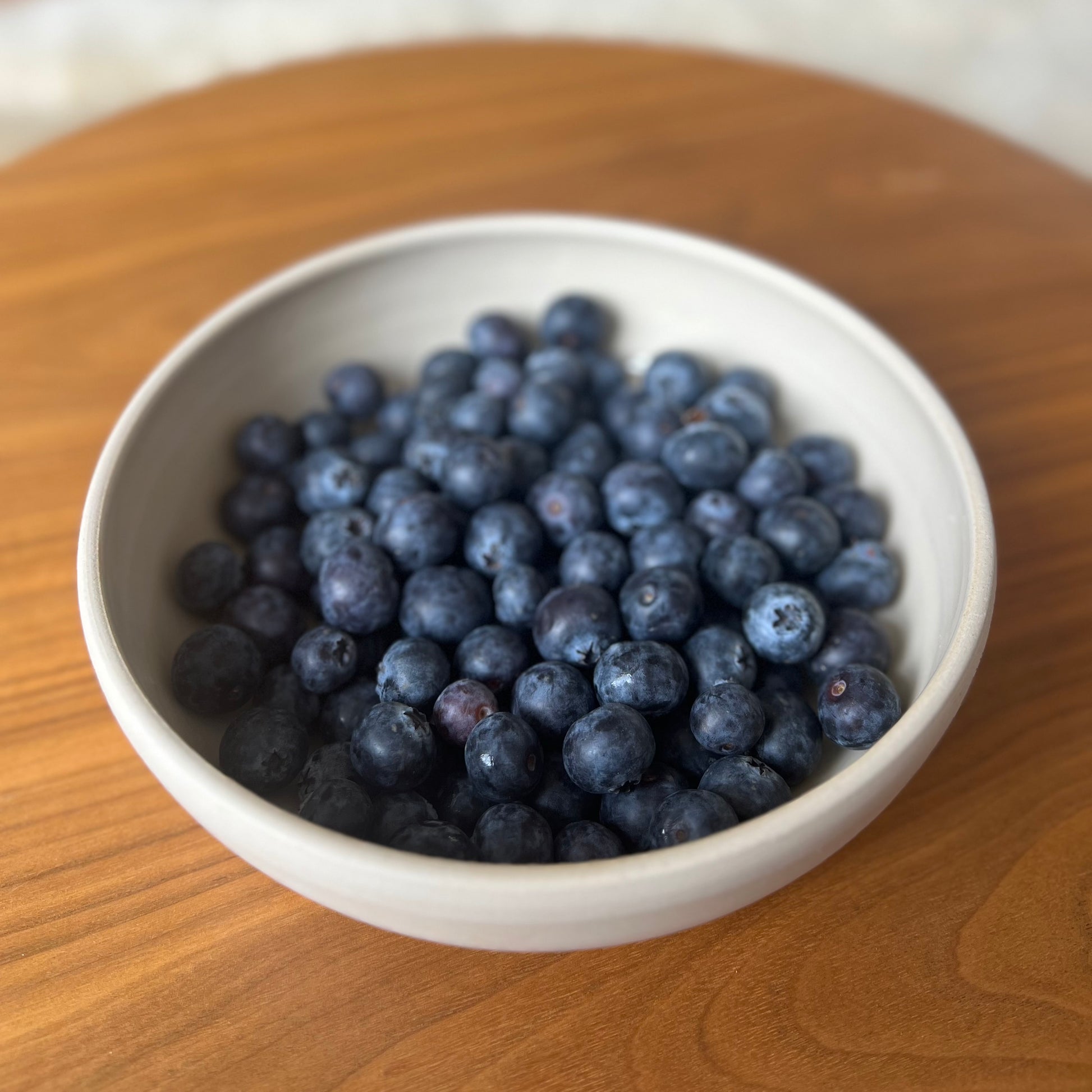 große flache beigefarbene handgedrehte Bowl aus Steinzeugton mit Blaubeeren gefüllt